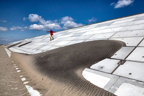 Image Caption: A woman makes her way down the seawall along the Kitakama and Ainokama coastline in Sendai, Japan. After the tsunami in 2011 the Japanese government has spent billions of yen on the reconstruction of a 31.8 km seawall along the Sendai coastline which is slated to be finished in 3 to 4 months. Commissioned photograph for the exhibition. ©Paula Bronstein.